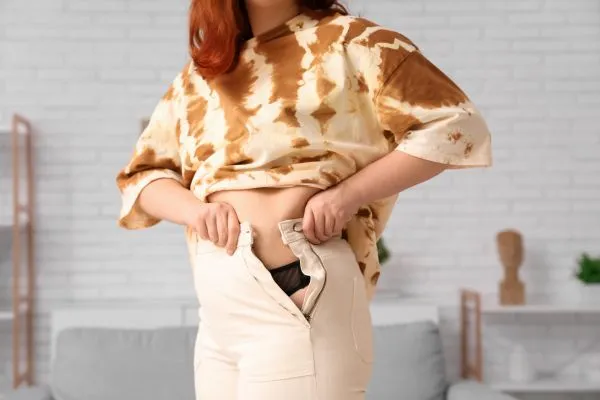 Image of woman trying to do her trousers up after pregnancy weight gain Feltham